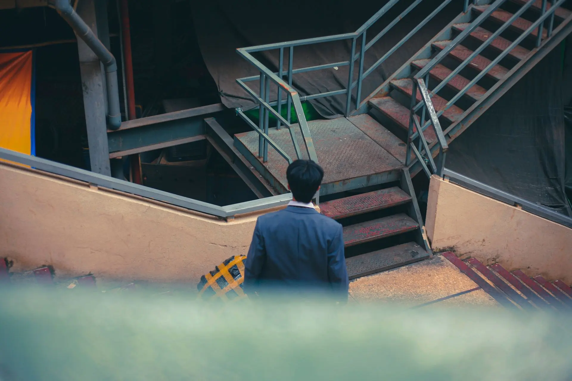 A man in a suit, seen from behind, walking up a metal staircase in the city.