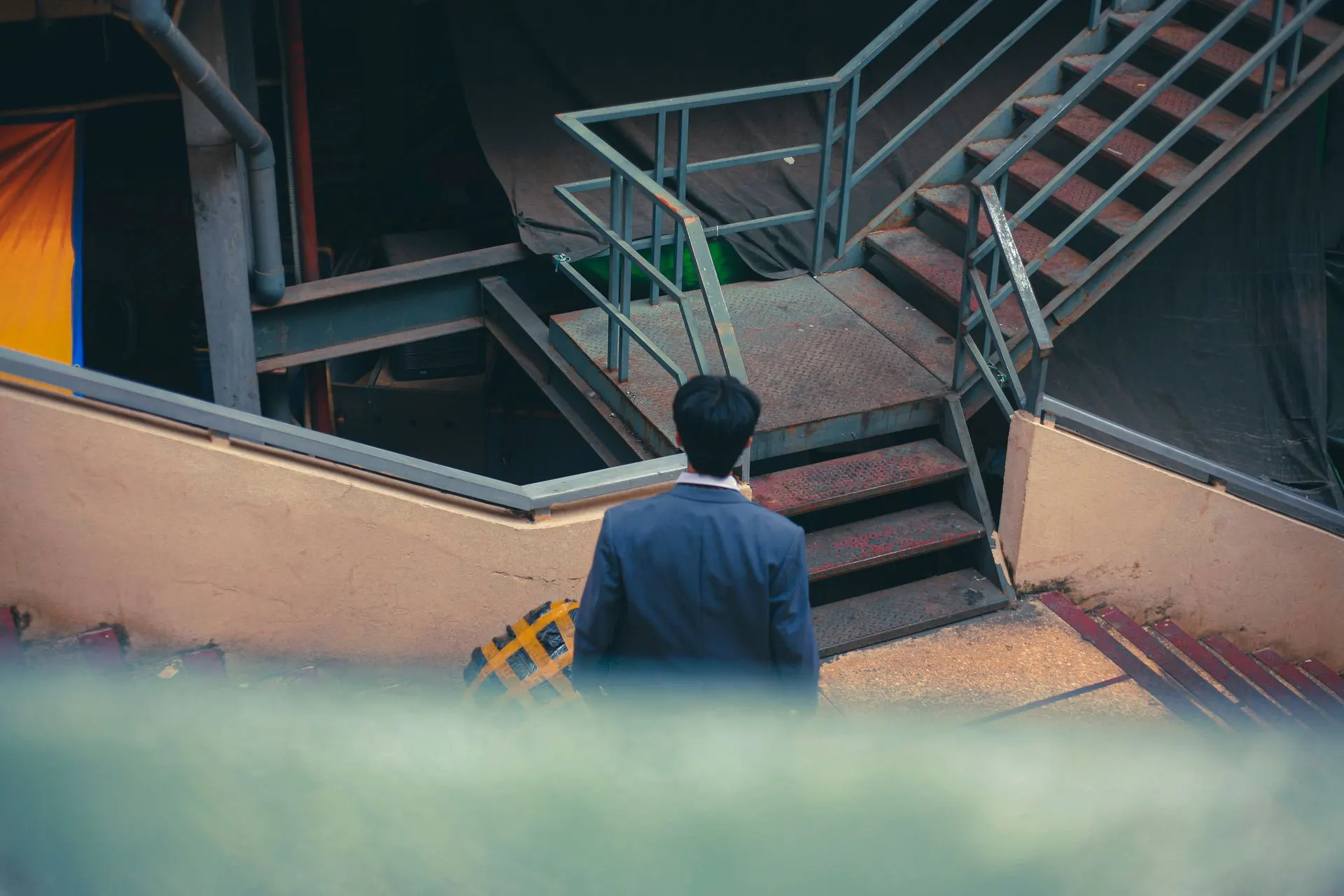 A man in a suit, seen from behind, walking up a metal staircase in the city.